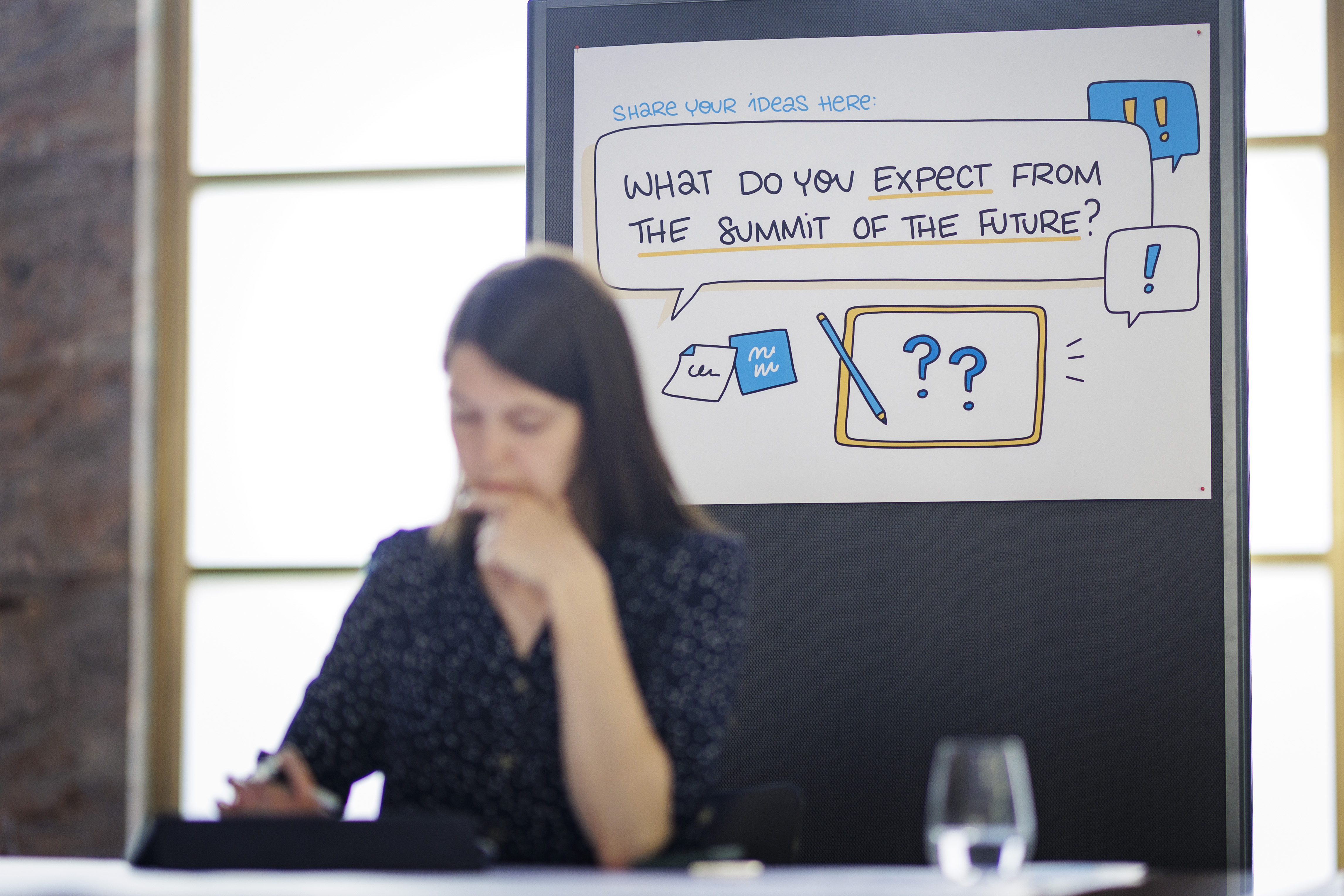 A person sitting in front of a banner reading "What do you expect from the Summit of the Future?"